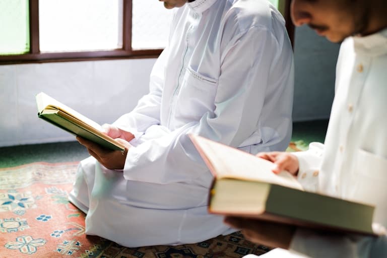 Two students sitting together, each reading from a muṣḥaf